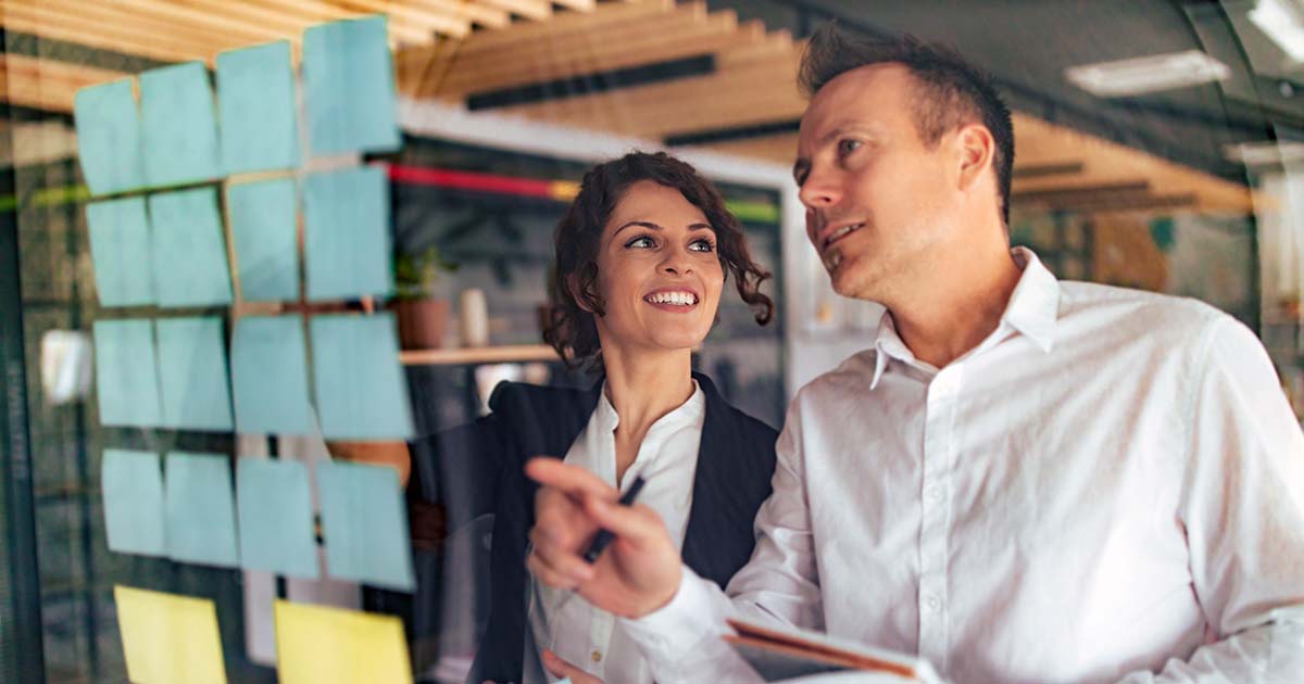 Professional man and woman planning using post-it notes on glass